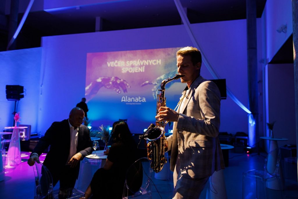 Saxofonista BURYSAX hraje na pódiu firemní konference s velkoplošnou projekcí